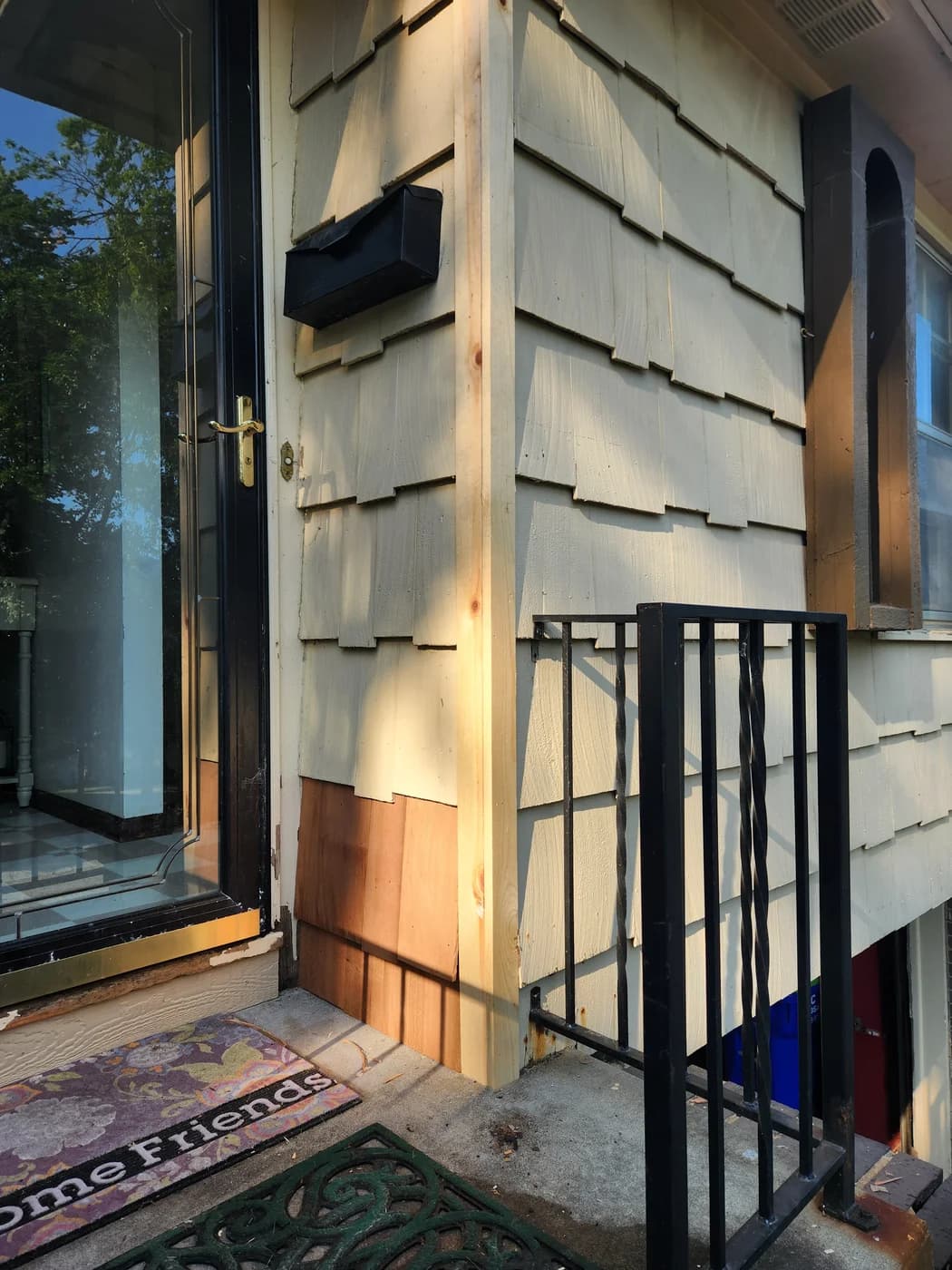 Replacement wood corner trim and shingles beside an entry door before painting